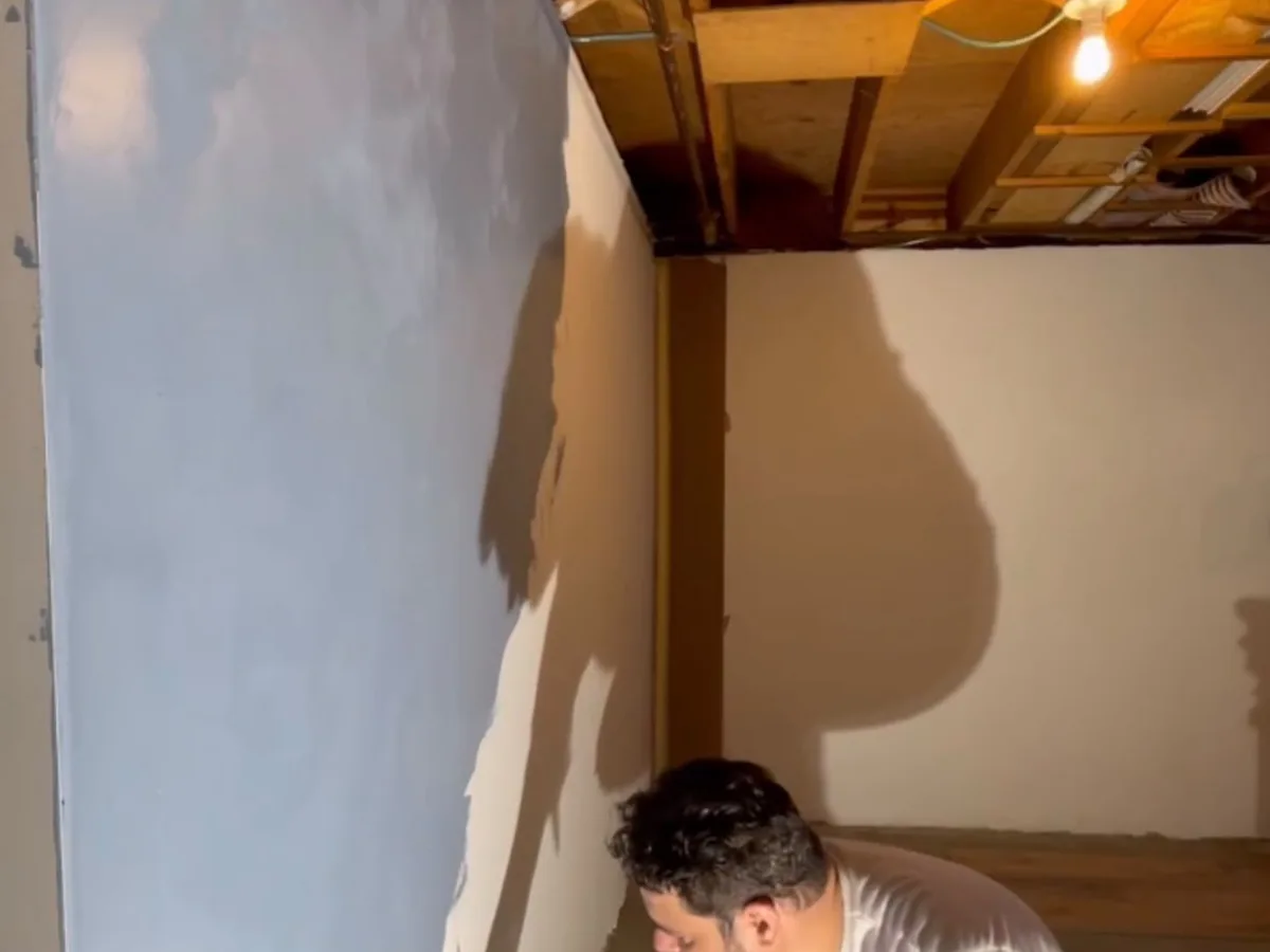 Plasterer working a fresh coat across a wall in an open framed room