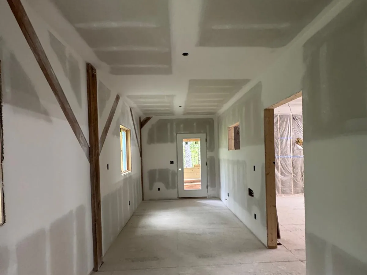 Drywall hung and taped along a corridor leading to a bright room