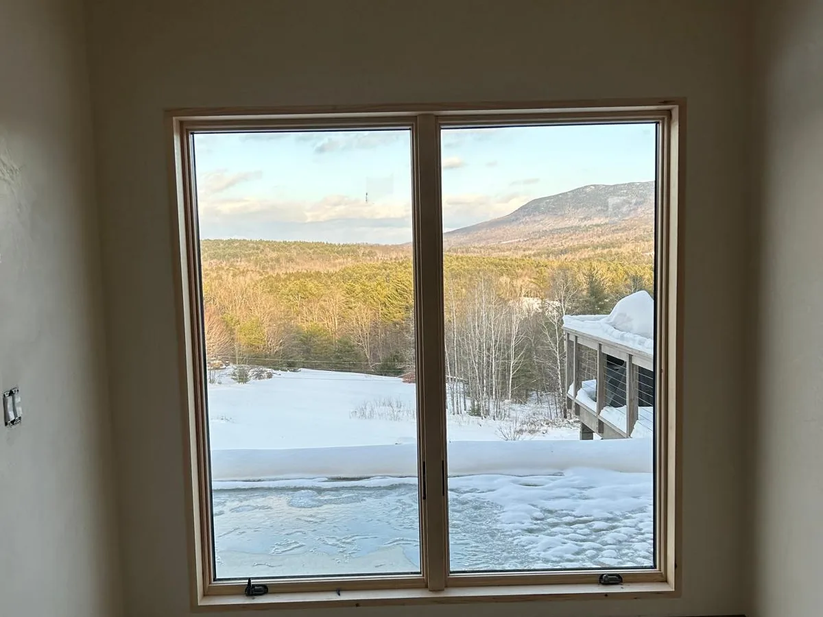 Plastered room with a large window framing a mountain view in winter