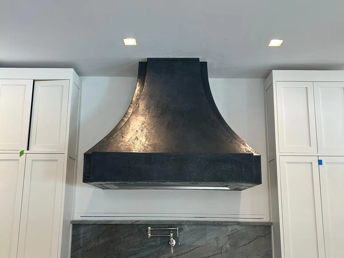 Custom dark plaster range hood over a professional range and a veined stone backsplash